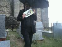 94. En un cementerio, vestido de duelo con un paraguas negro mientras llueve.