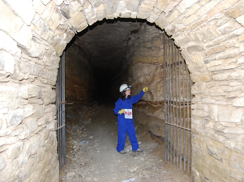 47. En la entrada de una mina o cueva, con un casco minero y un pico