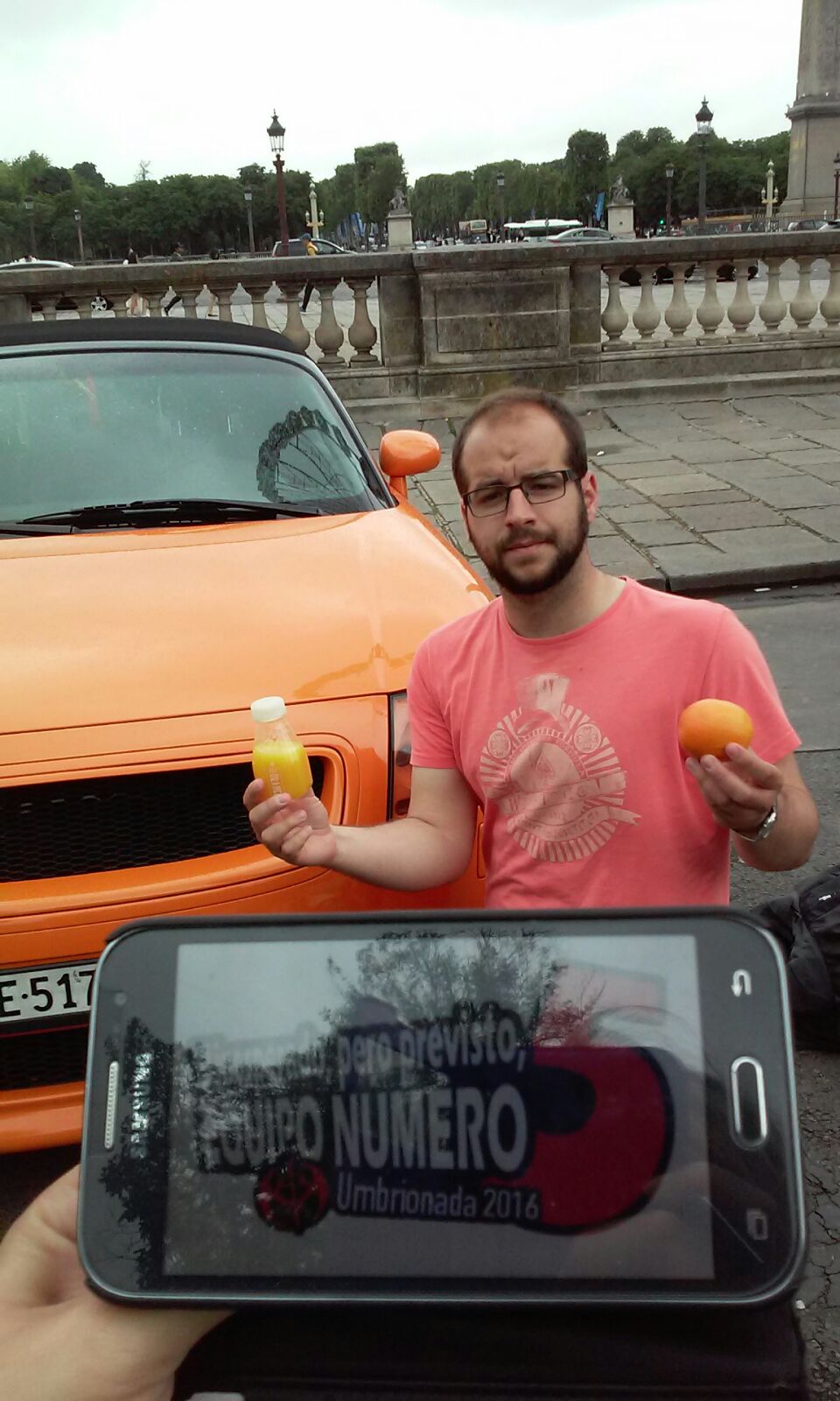 98. Junto a un coche naranja, vestido de color naranja, con una mano sujetando una naranja y con la otra bebiendo zumo de naranja.