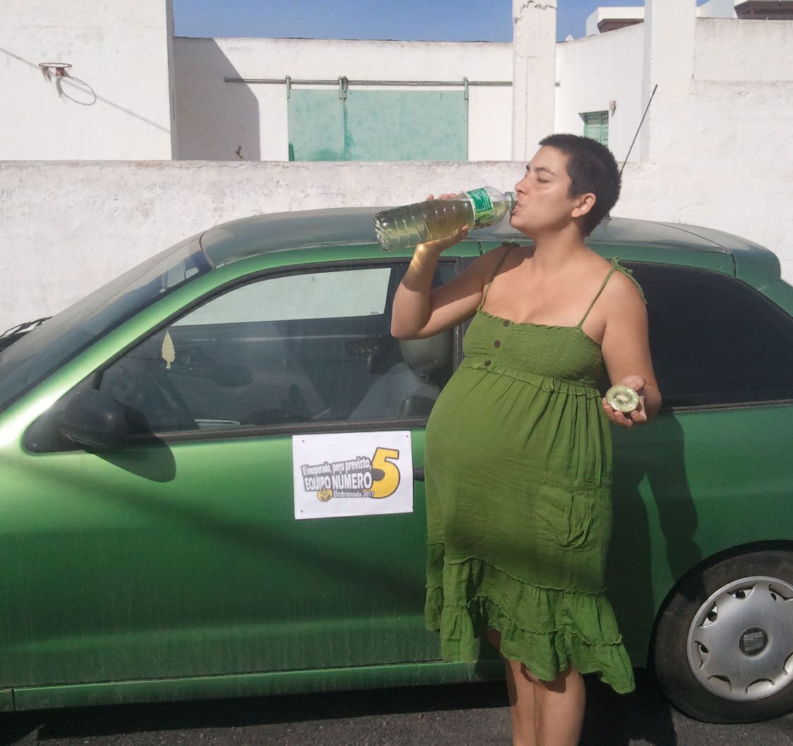 71. Junto a un coche verde, vestido de verde, tomando una bebida verde y mostrando medio kiwi por el lado verde.