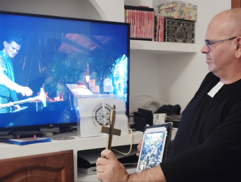 90 - Disfrazado de exorcista, con un manual de rol en la mano, haciendo un exorcismo a una pantalla donde se vea un fotograma de “Los anillos del pode