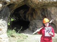 47. En la entrada de una mina o cueva, con un casco minero y un pico