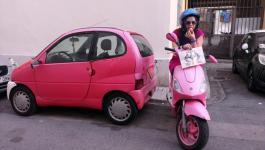 95. Vestido de color rosa, mientras te comes un bollito Pantera Rosa, junto a un coche rosa. 