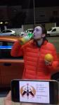98. Junto a un coche naranja, vestido de color naranja, con una mano sujetando una naranja y con la otra bebiendo zumo de naranja.
